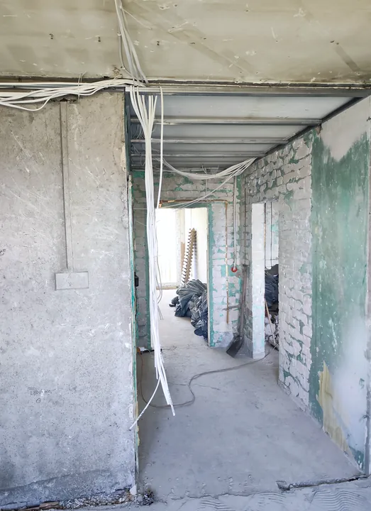 Przewody instalacji elektrycznej poprowadzone pod sufitem i przy przejściu między pomieszczeniami w mieszkaniu w Dąbrowie Górniczej.